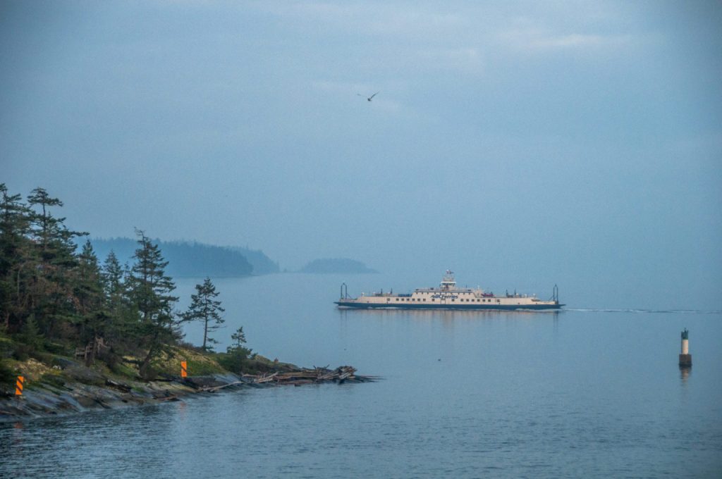 Ferry traversant un bras de mer brumeux bordé d'îlots couverts de conifères