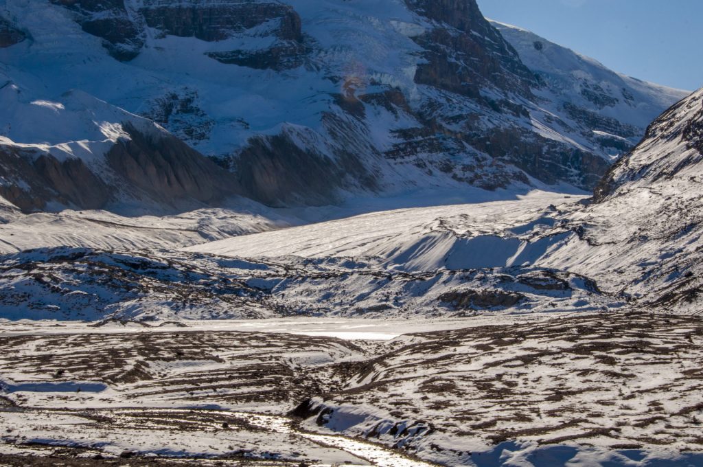 Langue d'un glacier descendant entre des parois enneigées jusqu'à une plaine de moraine