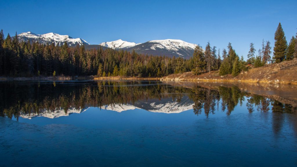 Montagnes enneigées et conifères se reflétant sur la surface lisse d'un lac gelé