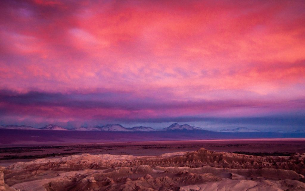 Ciel rose et violet embrasant les crêtes minérales de la Valle de la Luna au crépuscule