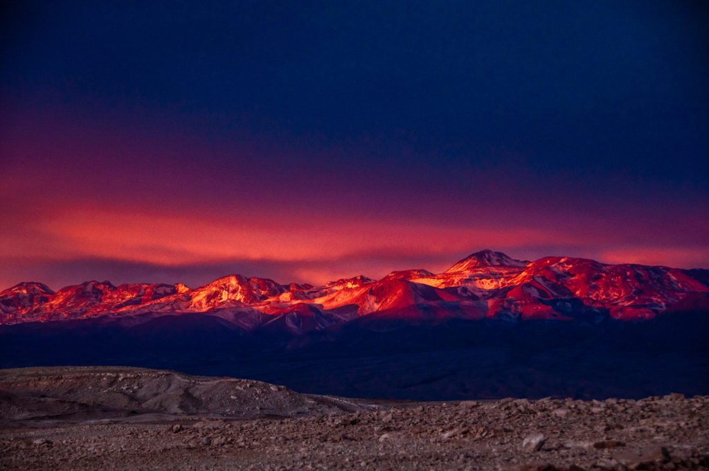 Crête andine enflammée par le dernier rayon sous un ciel bleu nuit, désert au premier plan