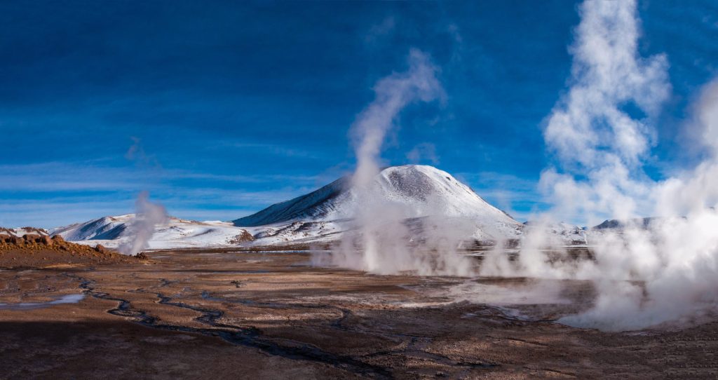 Panoramique du champ géothermal, colonnes de vapeur devant un volcan enneigé