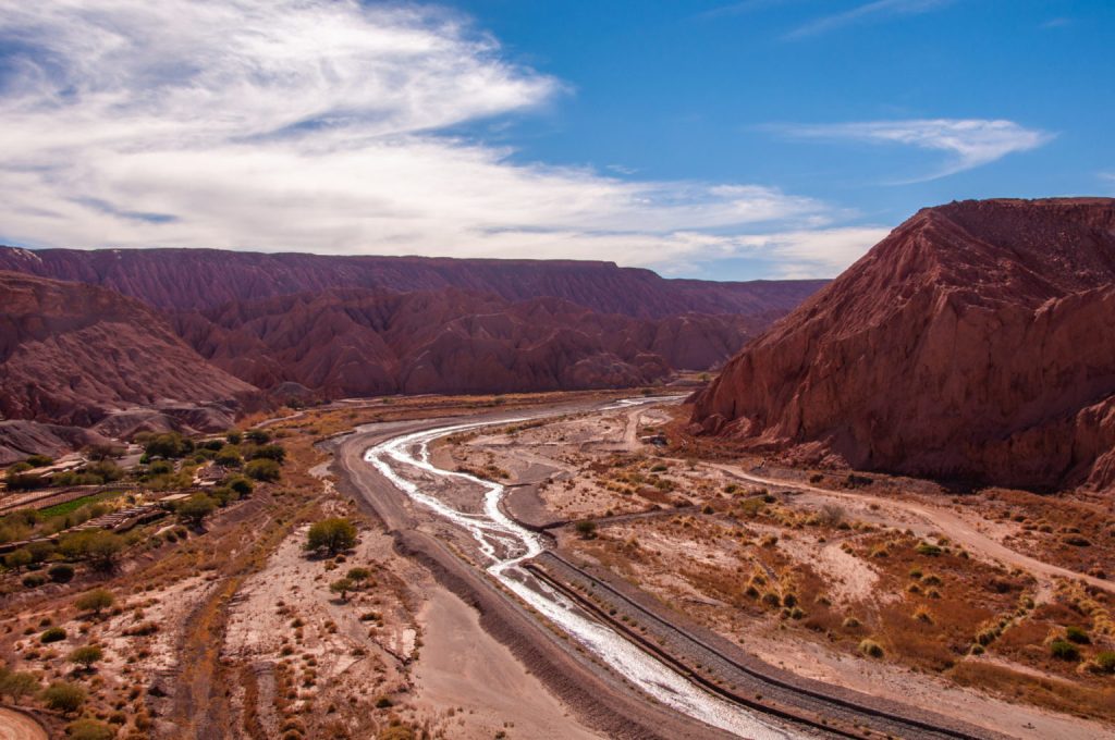 Rivière serpentant au fond d'un canyon de roche rouge, voie ferrée longeant la rive