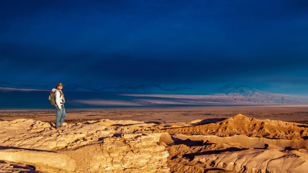 Randonneur debout sur une crête rocheuse dominant l'immensité du désert d'Atacama