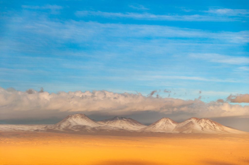 Ligne de volcans enneigés émergeant d'un plateau désertique doré sous un ciel bleu profond
