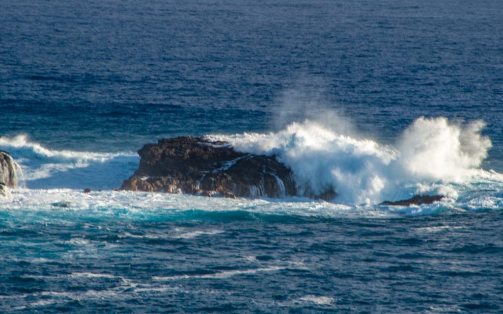 Vague puissante explosant en gerbe blanche contre un rocher noir en pleine mer