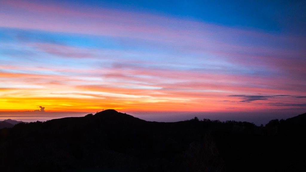 Bandes de nuages roses et oranges au-dessus d'une crête volcanique à contre-jour