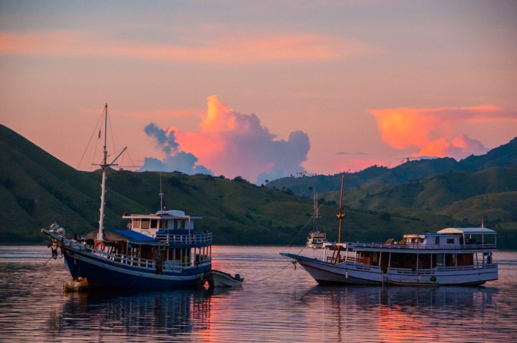 Deux bateaux traditionnels en bois au mouillage dans une baie, ciel et nuages roses