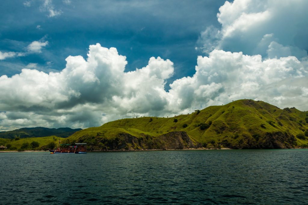 Collines herbeuses bordant une mer sombre sous d'imposants cumulus blancs, bateau amarré