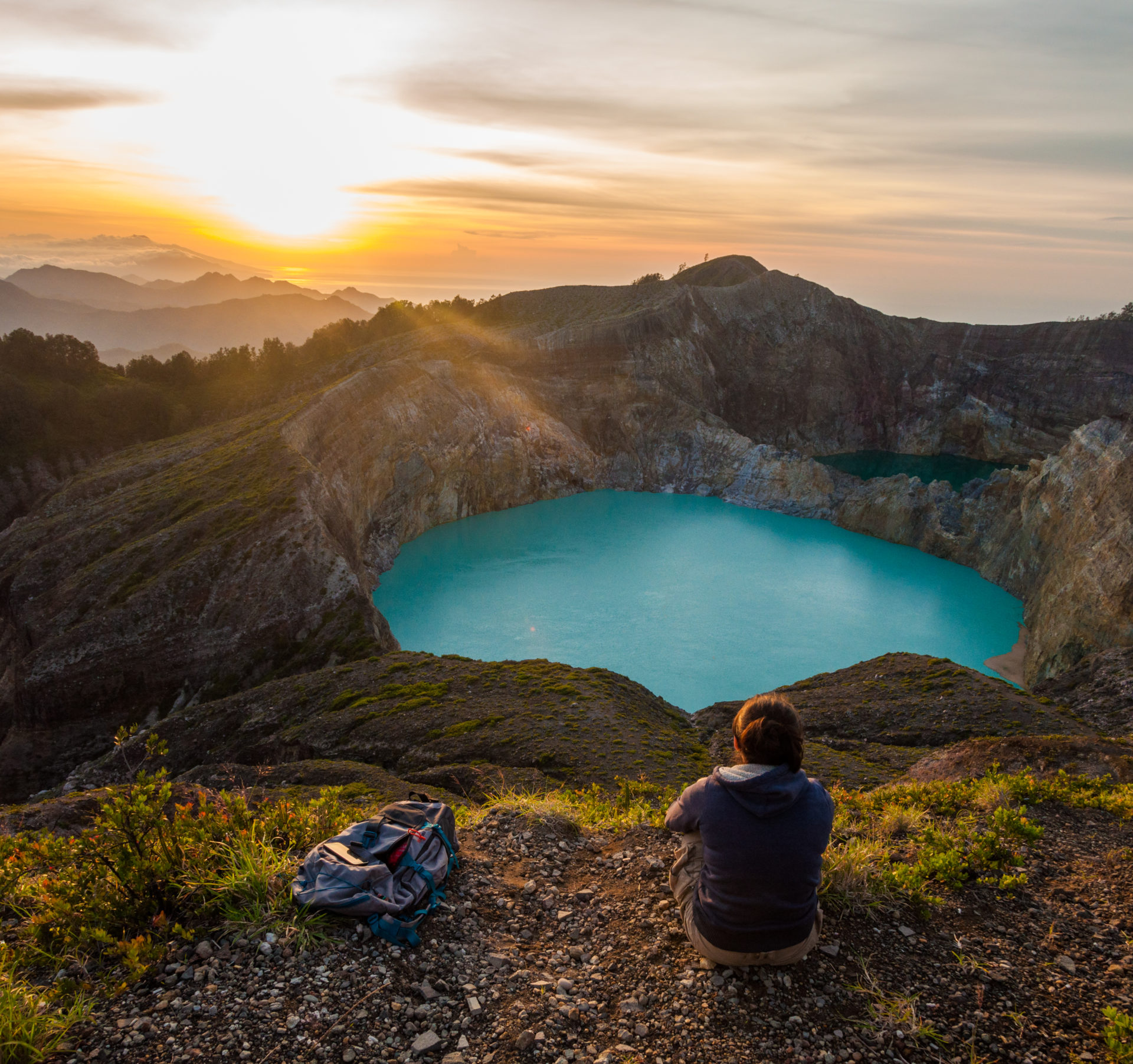 Voyageuse assise au bord du cratère contemplant le lac turquoise du Kelimutu au lever du soleil