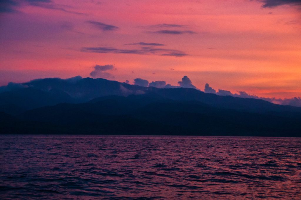Ciel rose et violet au crépuscule au-dessus d'une ligne de montagnes bleutées et d'une mer calme