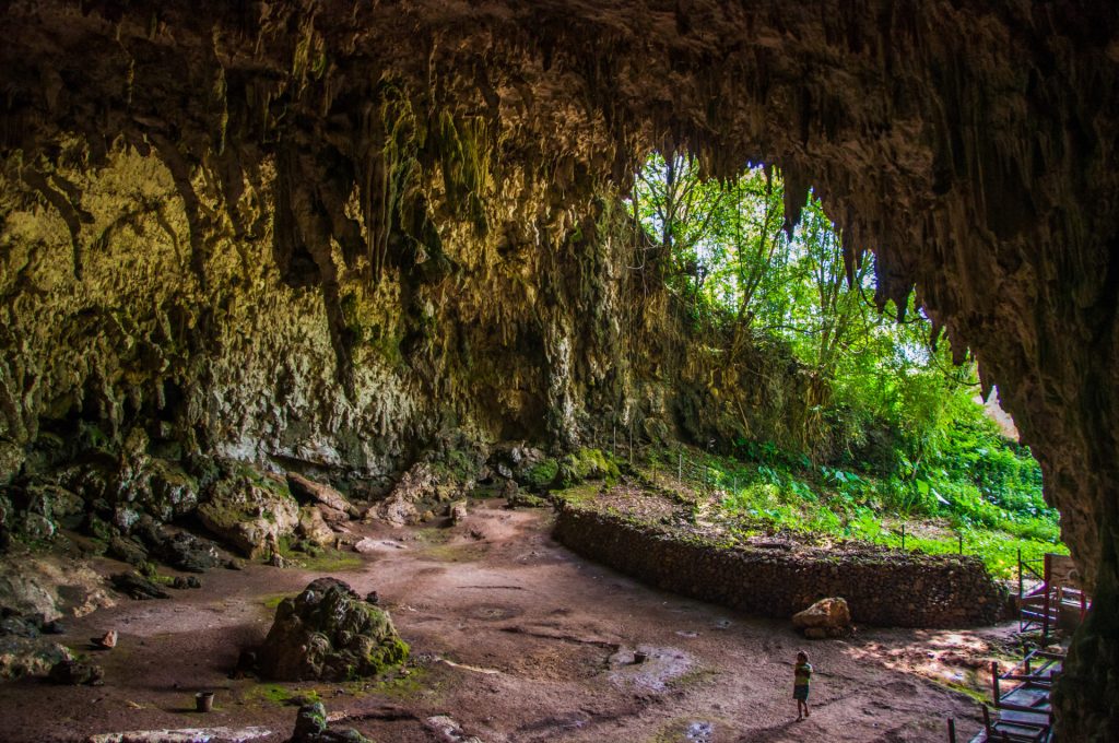 Vaste porche de grotte calcaire ouvert sur la jungle, silhouette minuscule pour l'échelle