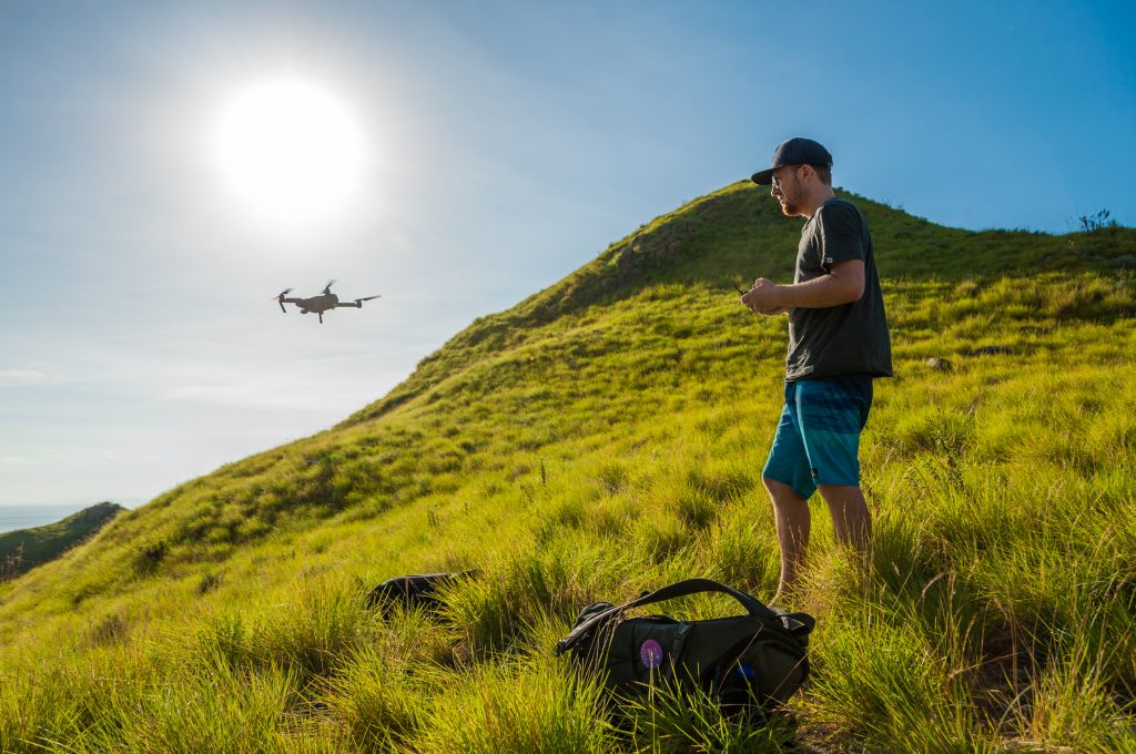 Photographe pilotant un drone depuis une colline d'herbe verte face à la mer