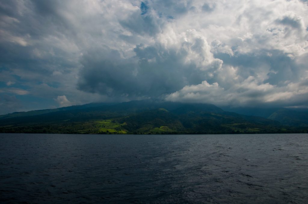 Front nuageux massif s'abattant sur des collines vertes bordant un grand lac sombre