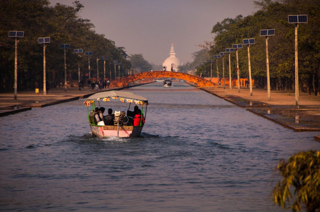 Barque remontant le canal de Lumbini vers un stupa blanc dans la lumière chaude du soir