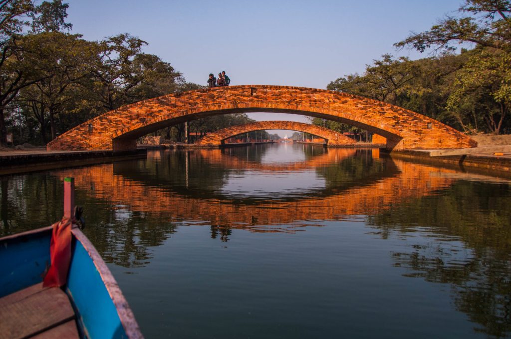 Pont de brique en arc se reflétant dans un canal calme, vu depuis la proue d'une barque