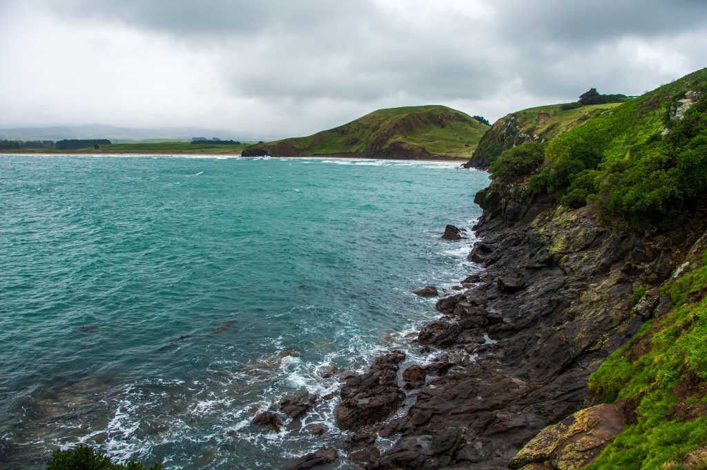 Falaises herbeuses plongeant dans une mer turquoise agitée sous un ciel chargé