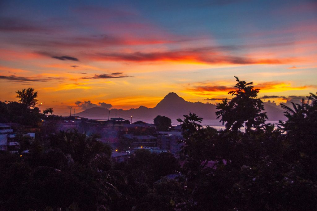 Ciel incandescent au-dessus de la silhouette d'une île montagneuse, végétation à contre-jour