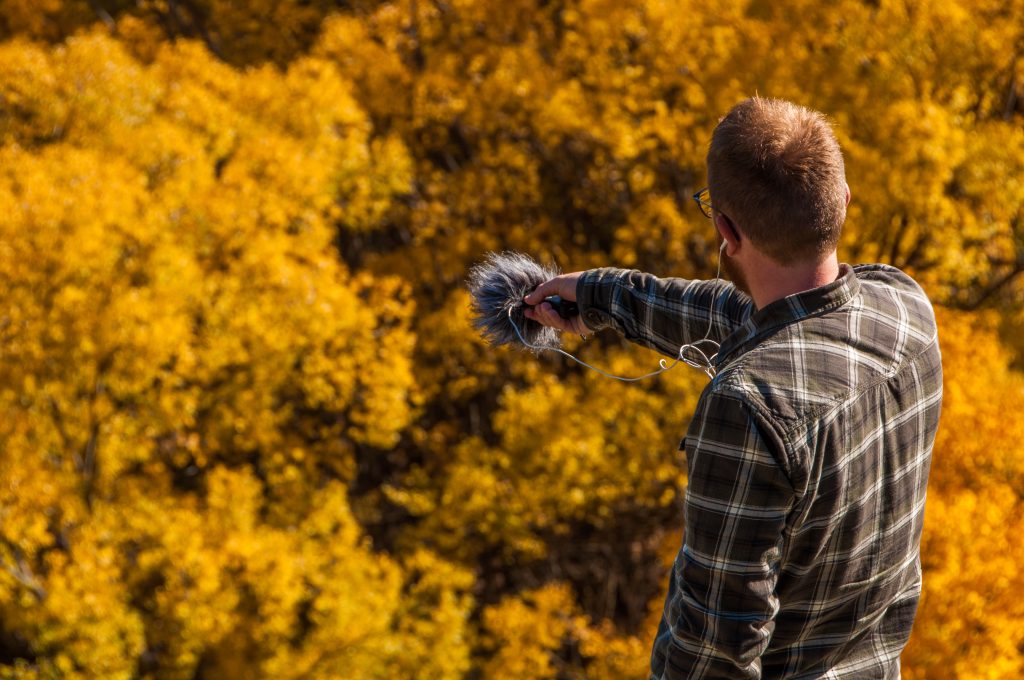 Preneur de son tendant un micro à bonnette vers une forêt aux feuillages dorés